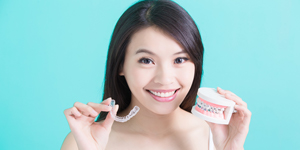 Woman holding Invisalign tray and model smile with braces